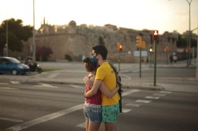 Una coppia di giovani ragazzi si abbraccia per strada con indosso la mascherina.