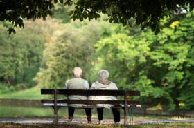 Una coppia anziana, ripresa di schiena, seduta su una panchina