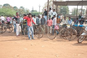 Gruppo di uomini, in prevalenza giovani, alcuni con la bicicletta, radunati nei pressi di una tettoia