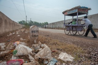 Un uomo spinge un carrello su una strada sterrata lungo la quale sono depositati rifiuti d ogni sorta