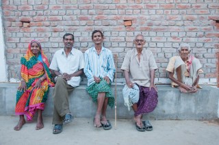 Famiglia seduta su un muretto davanti a una casa a mattoni, sorride alla camera