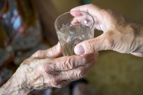 mani di un anziana che tengono un bicchiere