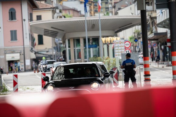 Posto di frontiera, con auto diretta dall Italia alla Svizzera e guardia, visto in lontananza; in primo piano transenna rossa