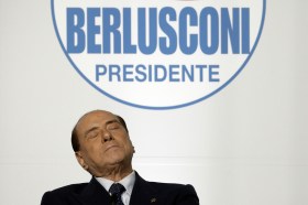 Silvio Berlusconi seduto leggermente reclinato all indietro e cogli occhi chiusi sotto il logo Berlusconi presidente