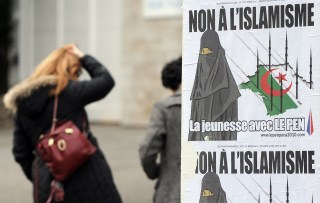 donna accanto a un manifesto con una persona col burqa e minareti a forma di missili