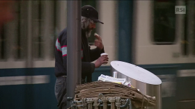 Uomo con berretto preleva da un cestino della spazzatura un alimento non completamente consumato.