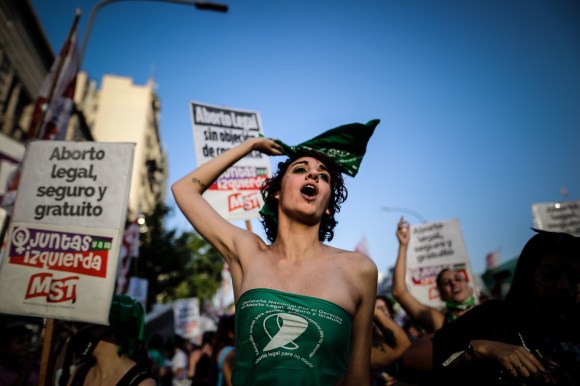 Una donna fasciata con un drappo verde manifesta circondata da cartelli pro-legge sull aborto