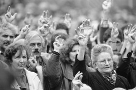 foto in bianco e nero: uomini e donne alzano la mano per votare