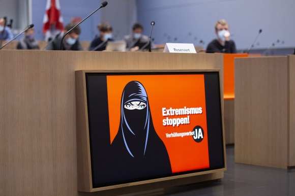Schermo posto su un banco di sala stampa mostra effige di donna col burqa e scritta Extremismus stoppen