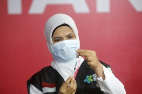 Donna con nijab e mascherina sanitaria dello stesso colore estrae vaccino da una fiala con una siringa