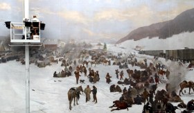 Restauratrice su un elevatore lavora a un grosso dipinto che raffigura uomini e cavalli in paesaggio alpino innevato