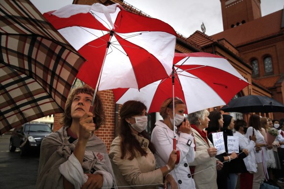 Fila di donna fuori da una chiesa, alcune con ombrello rosso-bianco, altre con cartelli di protesta
