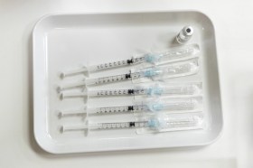 Vassoio medicale con cinque siringhe il cui ago è ancora coperto dalla confezione e fiala di vaccino