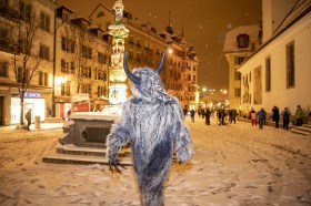 Persona travestita con pelliccia e corna finte passeggia di notte per la strada di un centro storico