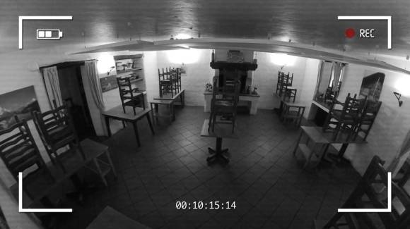 Immagine b/n di un ristorante vuoto con sedie sui tavoli; riquadro, icona batteria e tempo come nel mirino di una telecamera