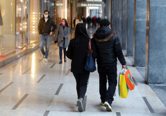 Due persone, di spalle, camminano in una via dello shopping con sacchetti colorati in mano