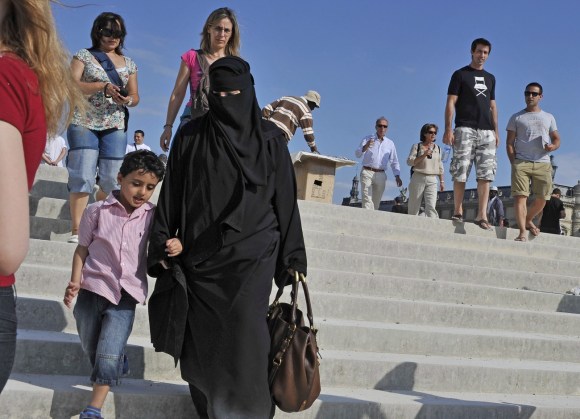 Una donna con il niqab scende da una scala accompagnata da un bambino