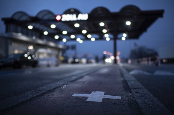 Immagine sfocata di un posto di frontiera al crepuscolo; si vedono bene luci e croce svizzera