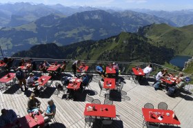 Terrazza di un ristorante con base in legno e tavoli rossi distanziati in ambiente alpino in altitudine
