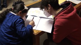 Una bambina seguita da un insegnante, mentre fa i compiti.
