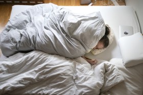 Una donna a letto sotto il piumone mentre consulta il proprio telefonino.