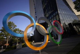 Insegna a forma di logo olimpico (cinque anelli colorati e intersecati) vista dal basso, accanto alla base di un grattacielo