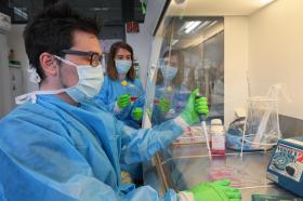 ricercatori con camice blu e mascherina mentre lavorano in laboratorio