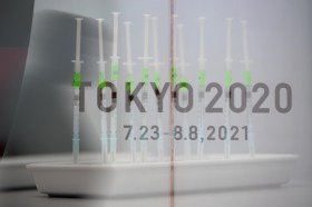 Il logo di Tokyo 2020 con sullo sfondo le siringhe del vaccino.