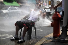un uomo seduta su una sedia si rinfresca con il getto d acqua che esce da un idrante