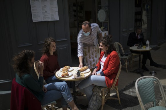 Un cameriere serve dei panini a tre ragazze sedute all esterno di un bar.