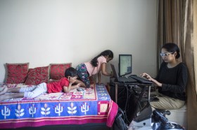 Una mamma lavora al computer con i suoi due bimbi davanti a lei sul letto.