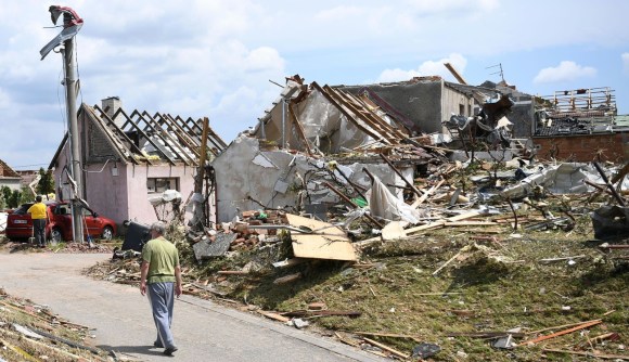 uomo cammina davanti alle macerie di due case, scoperchiate e semidistrutte dal tornado