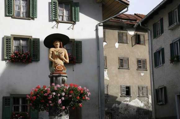 scorcio di un villaggio con statua di un uomo con cappello e facciate di due edifici