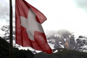 Una bandiera svizzera con sullo sfondo le montagne innevate del canton Uri in piena estate.