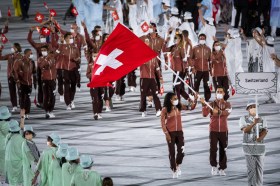 due atleti in mascherina (un uomo a una donna) sventolano la bandiera svizzera