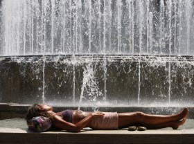 Donna sdraiata su una panchina con dietro una fontana.