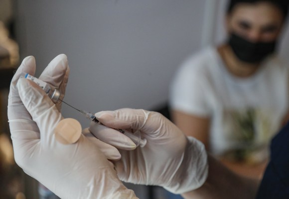 primo piano di mani con guanti che prelevano con una siringa da una fiala una dose di vaccino