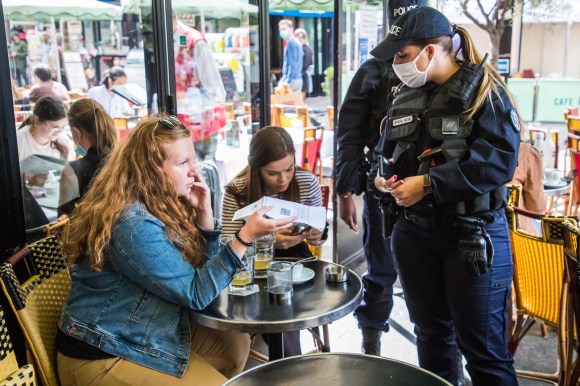 Una poliziotta francese controlla il certificato di una ragazza seduta in un bar.