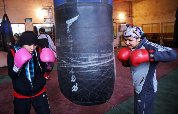 due donne afghane colpiscono un sacco da boxe, indossando guanti da boxe