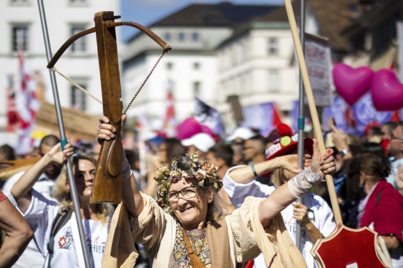 Donna con balestra e bandiera svizzera che manifesta contro le misure anti covid-19.