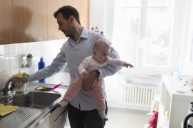Un uomo in cucina con in braccio un neonato.