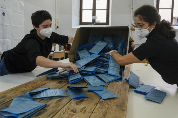 due donne con mascherina e guanti svuotano una scatola contenente schede elettorali blu