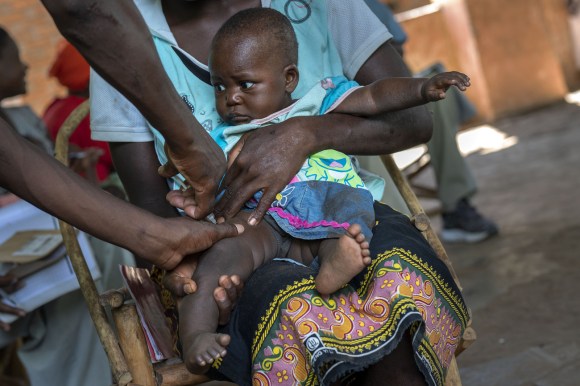 bambino africano tenuto in braccio dalal madre si fa somministrare un vaccino con puntura sulla gamba destra