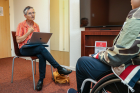 una donna seduta con un computer portatile parla con una persona ins edia a rotelle