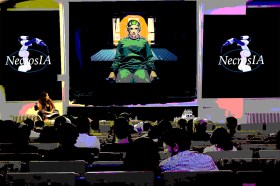 [illustrazione] Una sala conferenze con persone in platea, logo NecrosIA ai lati e una donna in sedia a rotelle sullo schermo