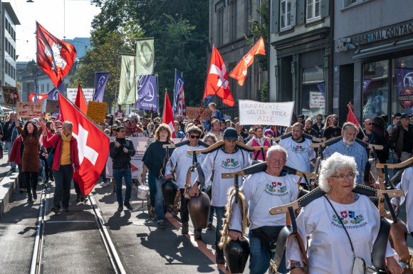 Gente in marcia con campanacci e bandiere svizzere.