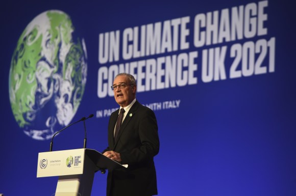 uomo parla da dietro un pulpito, dietro di lui scritta un climate change conference uk 2021 accanto immagine del pianeta terra