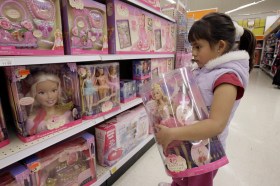 bambina tiene in mano scatola contenente una bambola mentre guarda altre bambole esposte in un negozio