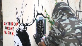 artista fotografato di spalle mentre spruzza spray nero su uno stencil