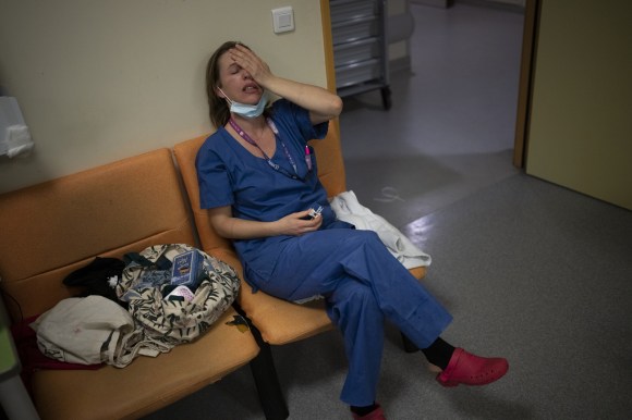infermiera seduta, vestita con completo blu, si mette una mano in faccia in segno di sfinimento